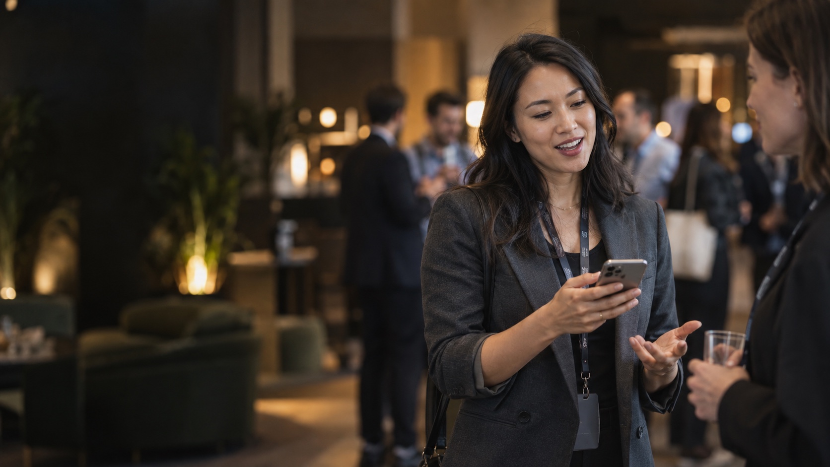 An Asian tech founder glances at her phone in one hand while networking at a tech conference.